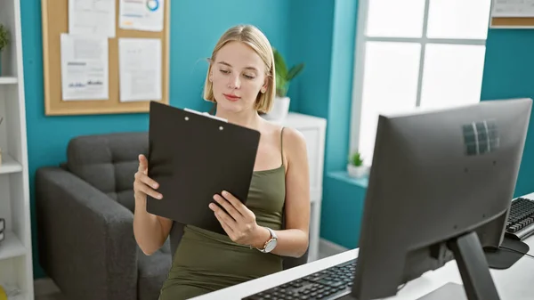 Young blonde woman business worker using computer reading document at the office