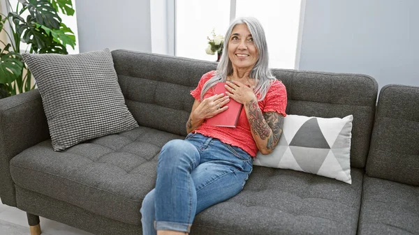 Evde, kendinden emin, gri saçlı, orta yaşlı bir kadın rahat kanepesinde oturuyor, elinde kitap, güzel gülüşü gerçek neşe ve rahatlık saçıyor..