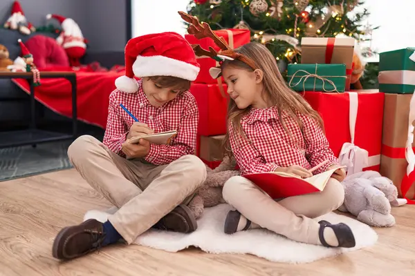 哥哥和姐姐在笔记本上画画 坐在家里的圣诞树旁 — 图库照片