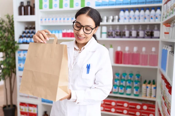 Young arab woman pharmacist smiling confident holding shopping bag at pharmacy