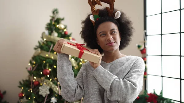 African american woman wearing reindeer ears listening christmas gift sound at home