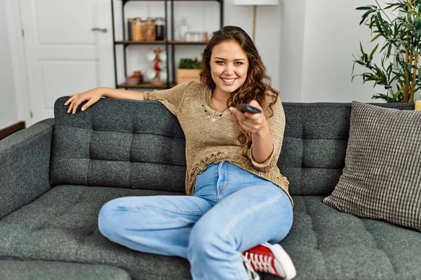 Young beautiful hispanic woman watching movie sitting on sofa at home