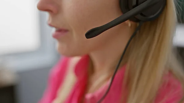 Close-up of a young blonde woman with a headset in a blurred office environment.