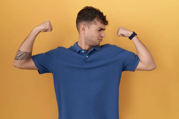 Ung Latinamerikansk Man Står Över Gul Bakgrund Visar Armar Muskler — Stockfoto
