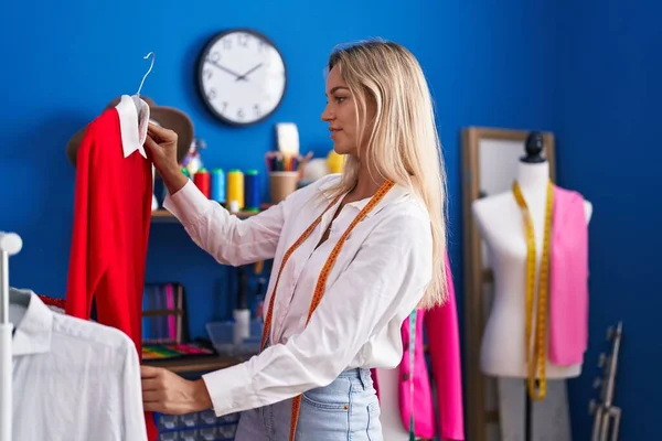 Young blonde woman tailor smiling confident holding clothes on rack at tailor shop