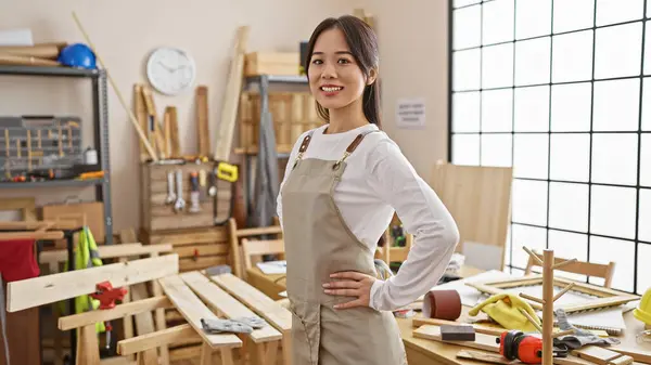 在设备齐全的木匠作坊里装腔作势的自信的亚洲年轻女子 — 图库照片