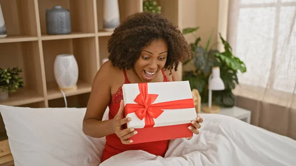 Excited african american woman holding a gift in a bedroom