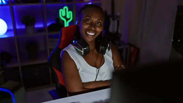 Smiling woman with headphones in a gaming room illuminated by neon lights at night, depicting leisure and technology.