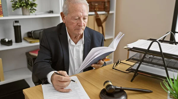 Senior man lawyer totally immersed in reading law book, taking notes in his office