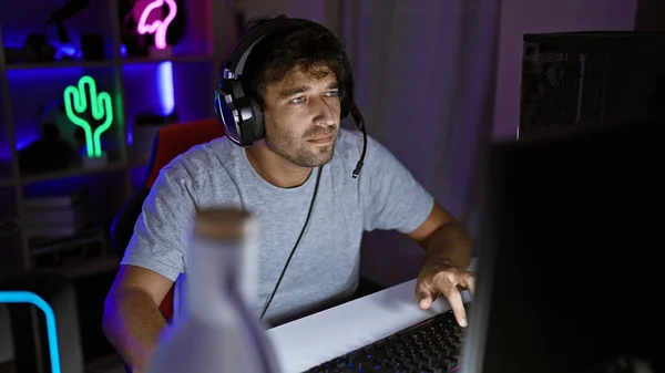 ヘッドフォンに焦点を当てた男性は 夜のネオンライトゲームルームでラップトップを使用しています — ストック写真