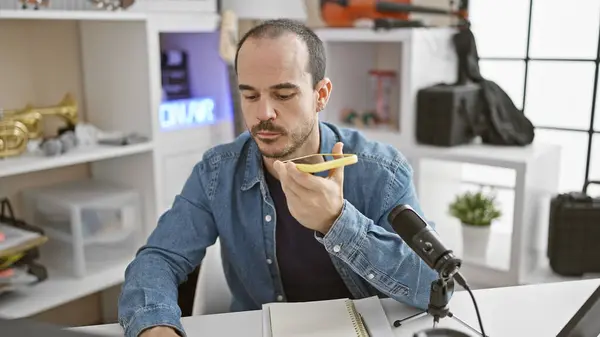 stock image Hispanic man with a beard recording in a music studio, speaking into phone while wearing casual attire indoors.