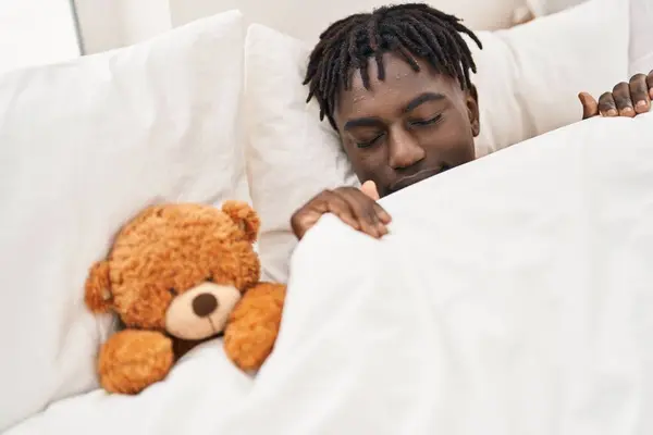 African american man lying on bed sleeping with teddy bear at bedroom