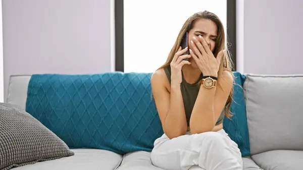 Attractive young hispanic woman\'s yawn interrupts phone convo while relaxed on sofa at home, seeming tired