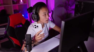 Akşamları renkli bir ofiste akıllı telefon ve oyun kulaklığı kullanan Asyalı bir kadın..