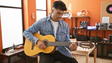 Genç bir İspanyol akustik gitar çalıyor. Kapalı bir müzik stüdyosunda dinleniyor..