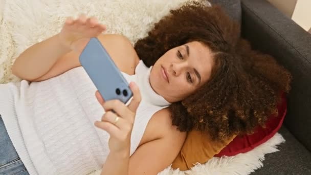 Genç Kıvırcık Saçlı Bir Kadın Akıllı Telefonuyla Evde Uzanıyor Rahat — Stok video
