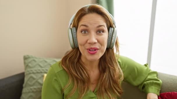 Wesoła Latynoska Kobieta Cieszy Się Muzyką Domu Nosząc Słuchawki Wygodną — Wideo stockowe