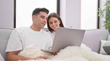 Gülümseyen bir kadın ve bir adam oturma odasında sarılıp kanepede dizüstü bilgisayara baktılar.