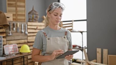 Güvenlik gözlüklü odaklanmış bir marangoz, iyi donanımlı bir marangoz atölyesinde tablet kullanır..