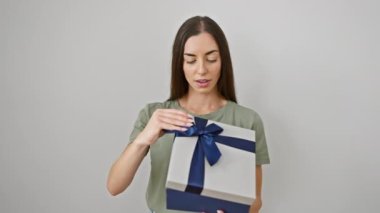 Beyaz karantinadaki stresli genç İspanyol kadın, elinde hediye paketi - öfke, sürpriz, doğum günü sorunu ile ilgili hayal kırıklığı, üzüntü duvarı ve karışık duygular