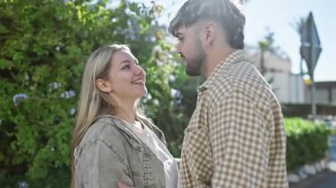 Genç bir adam ve bir kadın açık havada kucaklaşıyorlar, güneşli bir parkta yemyeşil ile çevrili bir anı paylaşıyorlar..