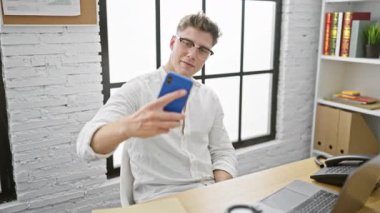 Yakışıklı beyaz bir adam, kendine güvenen bir iş adamı, akıllı telefonuyla eğlenceli bir selfie çekiyor, zarif ofis masasına gülümsüyor..