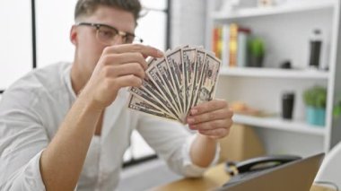 Yakışıklı beyaz iş adamı ofisinde oturmuş, ciddi ciddi dolar banknotlarını sayıyor, başarılı bir yatırım başarısı.!