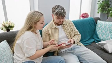 Kadın ve erkek rahat oturma odasındaki koltukta akıllı telefonları kullanarak modern çiftlerin boş zamanlarını resmediyorlar..