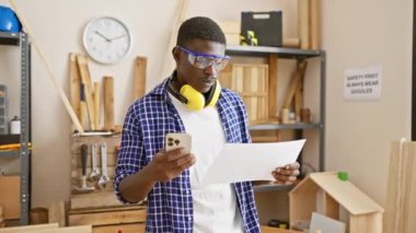 Marangozluk atölyesinde akıllı telefon ve güvenlik gözlüğü olan yakışıklı bir adam.