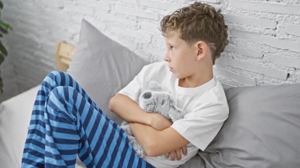 Adorable Niño Rubio Pijama Sentado Cama Dormitorio Abrazando Oso Peluche — Vídeo de stock