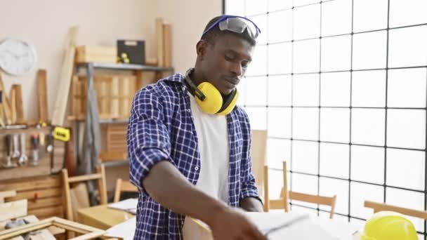 Afrikanischer Mann Untersucht Baupläne Einer Sonnendurchfluteten Tischlerei Die Handwerkskunst Und — Stockvideo