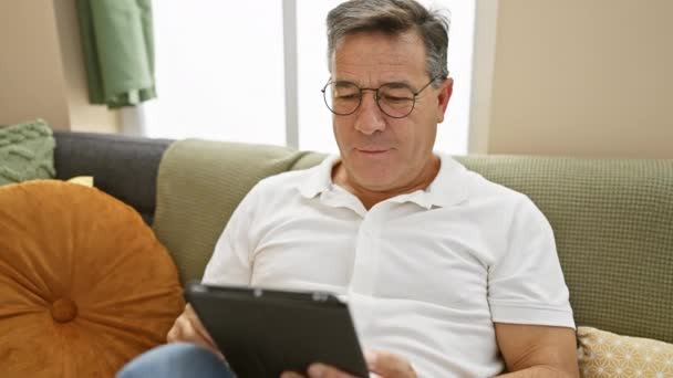 自宅でソファーでタブレットを使用してメガネで成熟した男 — ストック動画