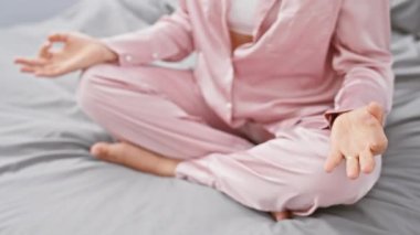 Kıvırcık saçlı genç bir İspanyol kadın huzurlu bir yatak odasında meditasyon yapıyor. Huzur ve kendine özen gösteriyor..