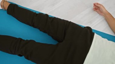 Rahatlamak ya da egzersiz yapmak için mavi yoga minderinde uzanan günlük kıyafetli sakallı genç bir adam.