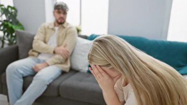 Endişeli bir adamla oturma odasında ağlayan bir kadın arkada oturuyor, ilişki sorunları tasvir ediyor..