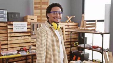 İyi donanımlı bir atölyede elinde matkap gözlüğü olan gülümseyen bir zanaatkar.