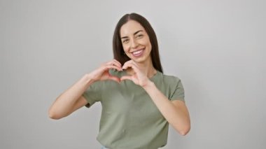 Göz alıcı İspanyol kadın, günlük giysiler içinde. Sevgisini ifade eden elleriyle kalp şekli çiziyor. Beyaz arka planda izole edilmiş romantik bir kavram.