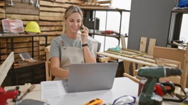 Genç bir kadın dizüstü bilgisayarında iyi donanımlı bir marangozluk atölyesinde çalışıyor..