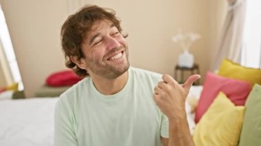 Neşeli, kendine güveni tam beyaz bir adam, neşeli bir şekilde yan tarafı işaret ediyor, parmakları havada, rahat yatak odası kıyafetleri içinde! Arsız, yakışıklı bakışlarıyla ışıl ışıl parlıyor..