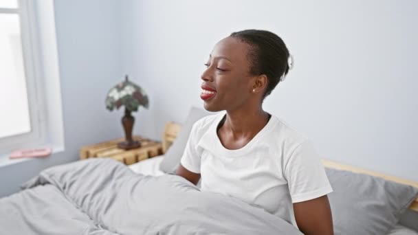 自信を持ったアフリカ系アメリカ人女性が髪に触れ 笑顔で寝室のベッドにファッショナブルにポーズ — ストック動画