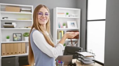 Heyecanlı genç sarışın iş kadını, neşeli bir şekilde bir kenara işaret ederek, açık avuçlarıyla fotokopi alanını gösteriyor, ofiste neşeli bir gülümsemeyle reklam sunuyor.