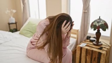 Yatak odasında elleri başında oturan üzgün kadın, rahat bir evde stres, endişe ya da baş ağrısı gösteriyor..