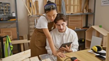 İki marangoz, bir erkek ve bir kadın bir marangoz, bir marangoz stüdyosunda iş birliği yapıyor, tablet üzerindeki planları inceliyorlar..
