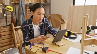 Marangozluk aletleriyle dolu bir atölyede akıllı telefon kullanan odaklanmış Asyalı bir kadın..