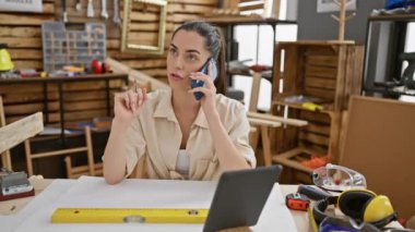 Genç, güzel İspanyol kadın marangoz, marangozluk atölyesinde kereste ve ahşap atölyesinde otururken akıllı telefonuyla canlı bir sohbete daldı.