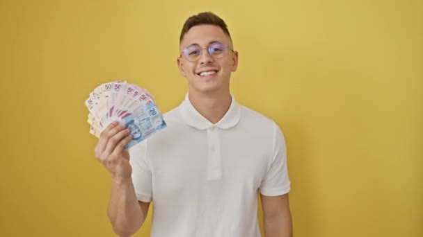 メキシコのペソ紙幣に喜ばれるチラシの若いヒスパニックな男は ポジティブな態度で明るく輝き 孤立した黄色の背景に自信を放射します — ストック動画