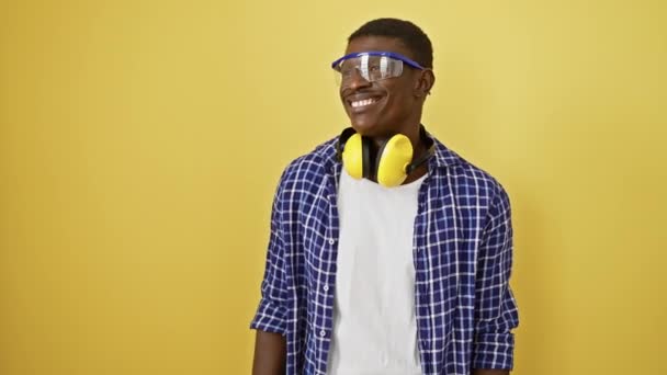 安全眼鏡を持った自信を持ったアフリカ系アメリカ人男性は笑い 横を向いて 黄色い隔離された背景に対して自然な表情を揺さぶります — ストック動画