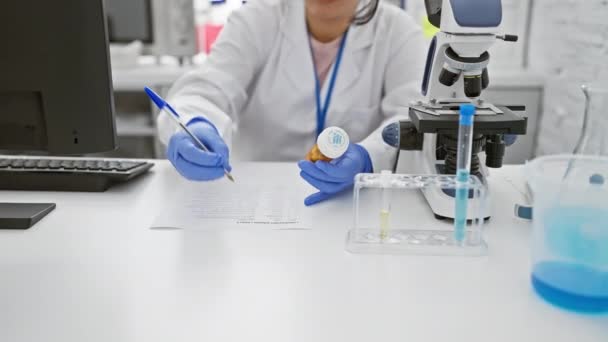 Focused Hispanic Woman Scientist Examines Medication Bottle Laboratory Microscope Test — Stock Video