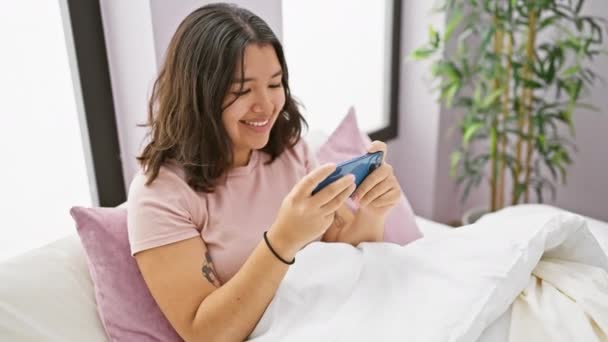 Mujer Hispana Riendo Mientras Juega Smartphone Dormitorio Luminoso — Vídeos de Stock