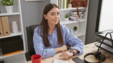Ofiste, genç ve güzel bir İspanyol kadın pozitif enerji yayarak kendini işaret ediyor. Gülümseyen yüzü, kendini beğenmiş ve gururlu ifadesi, iyimserlikle parlıyor..